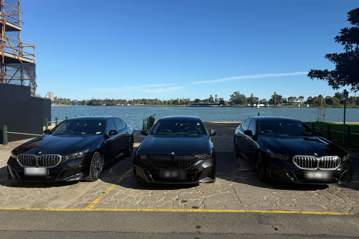 Three black BMW 5 Series chauffeur cars parked side by side by the water