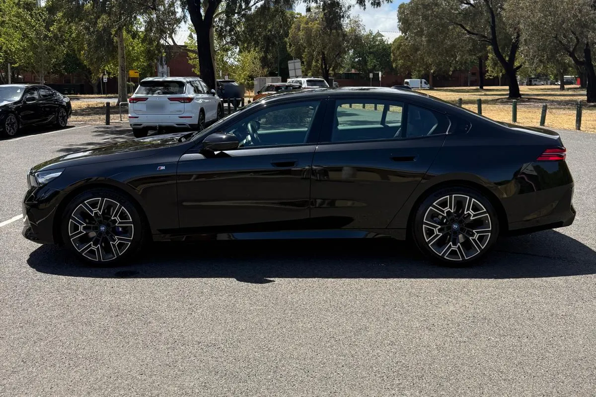 Black BMW 5 Series chauffeur car seen from the side under gum trees