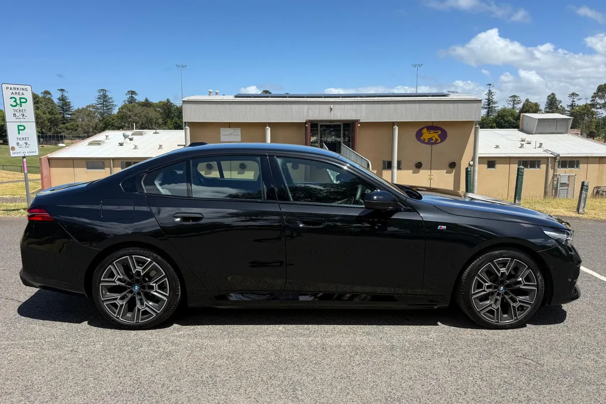Side profile of a black BMW 5 Series chauffeur car in an open car park