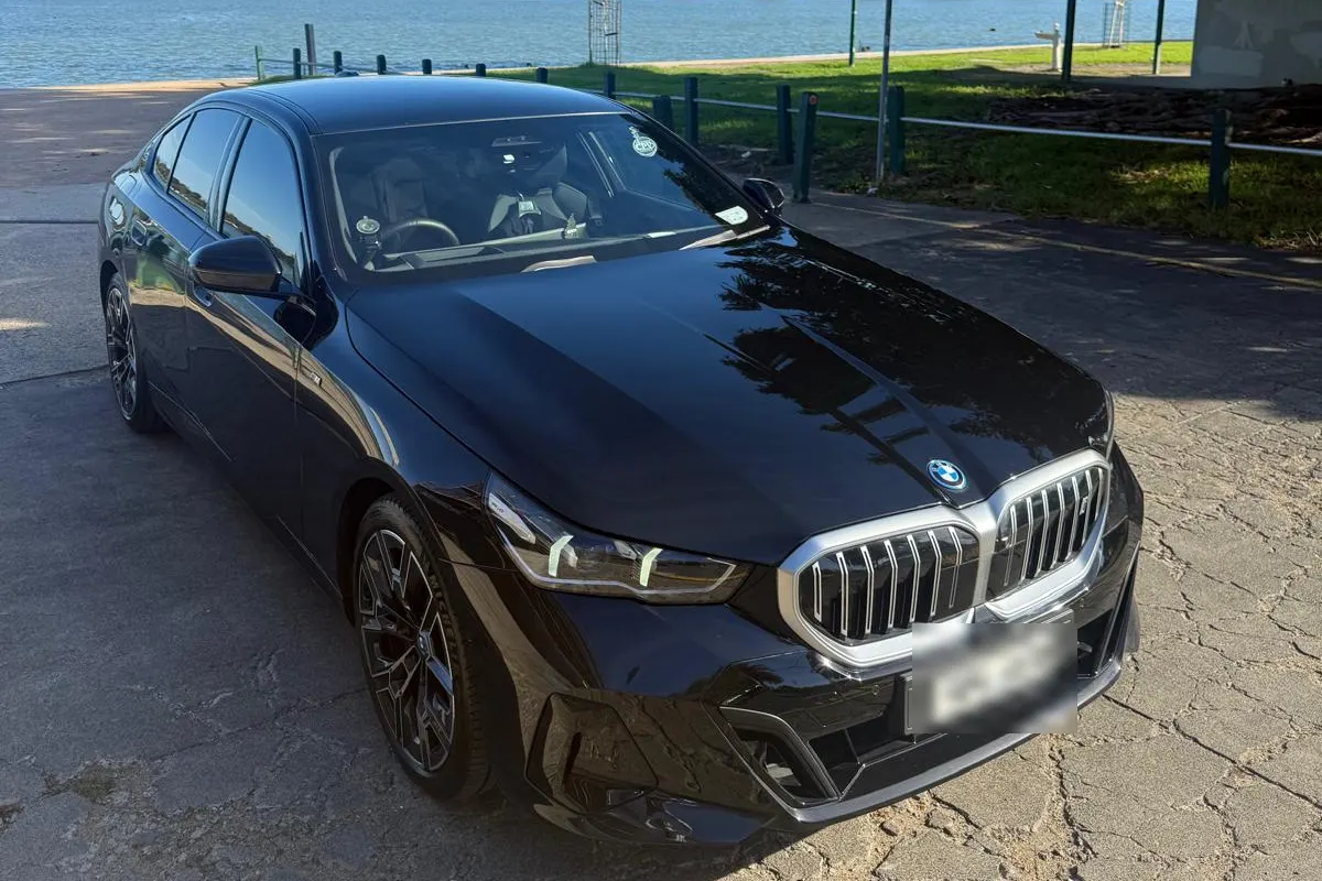 Black BMW 5 Series chauffeur car parked by the water, seen from the front corner
