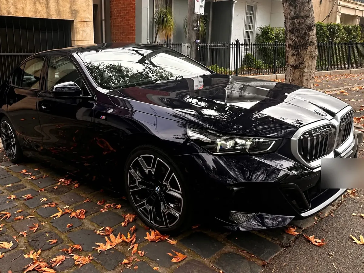 Black BMW i5 chauffeur car parked on a cobbled Melbourne street with autumn leaves