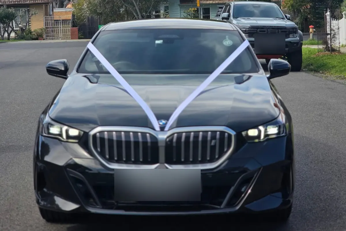 Black BMW 5 Series dressed with white wedding ribbon across the bonnet